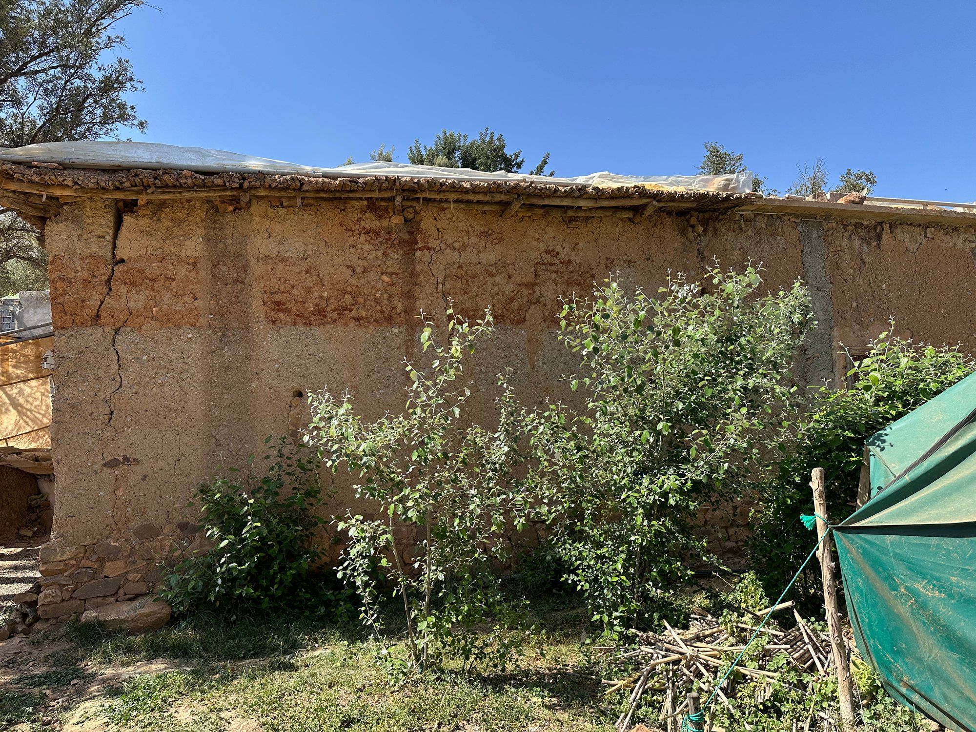 A long rammed-earth wall with a diagonal earthquake crack, its roof under a temporary tarp during repair, in the High Atlas.