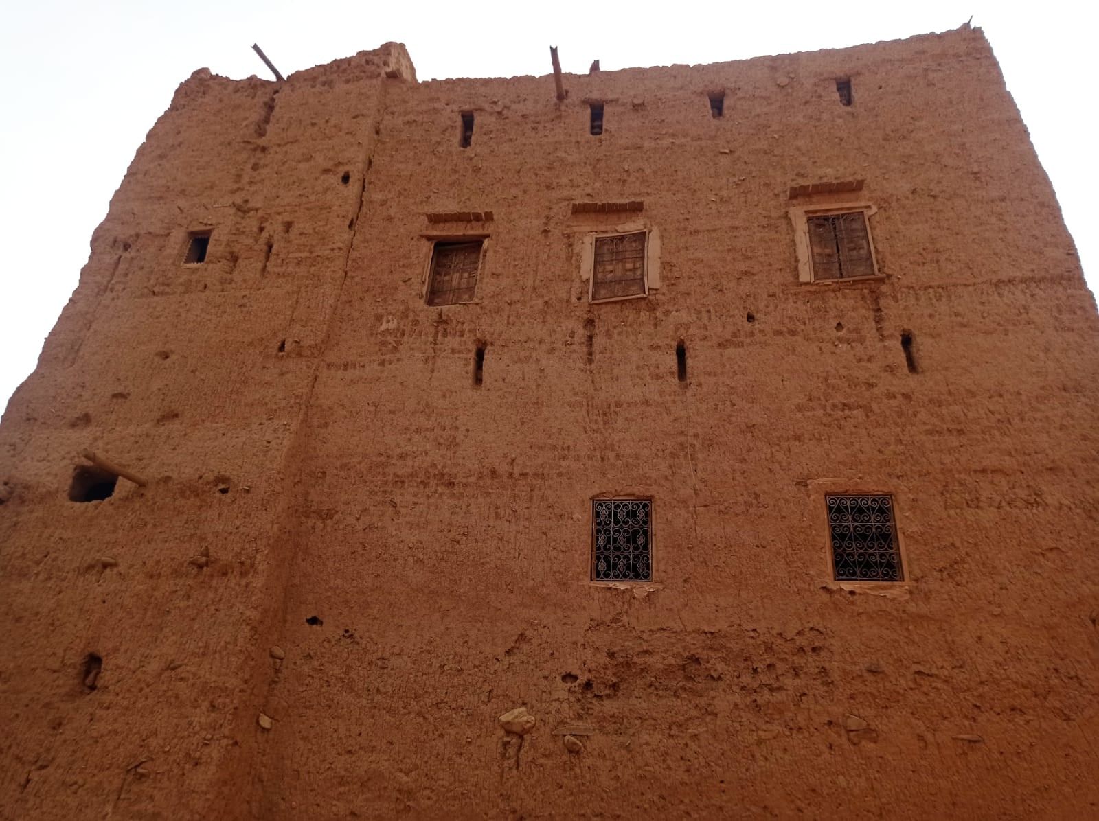 A tall rammed-earth facade in Tazarine seen from below, its windows set deep into the ochre wall.